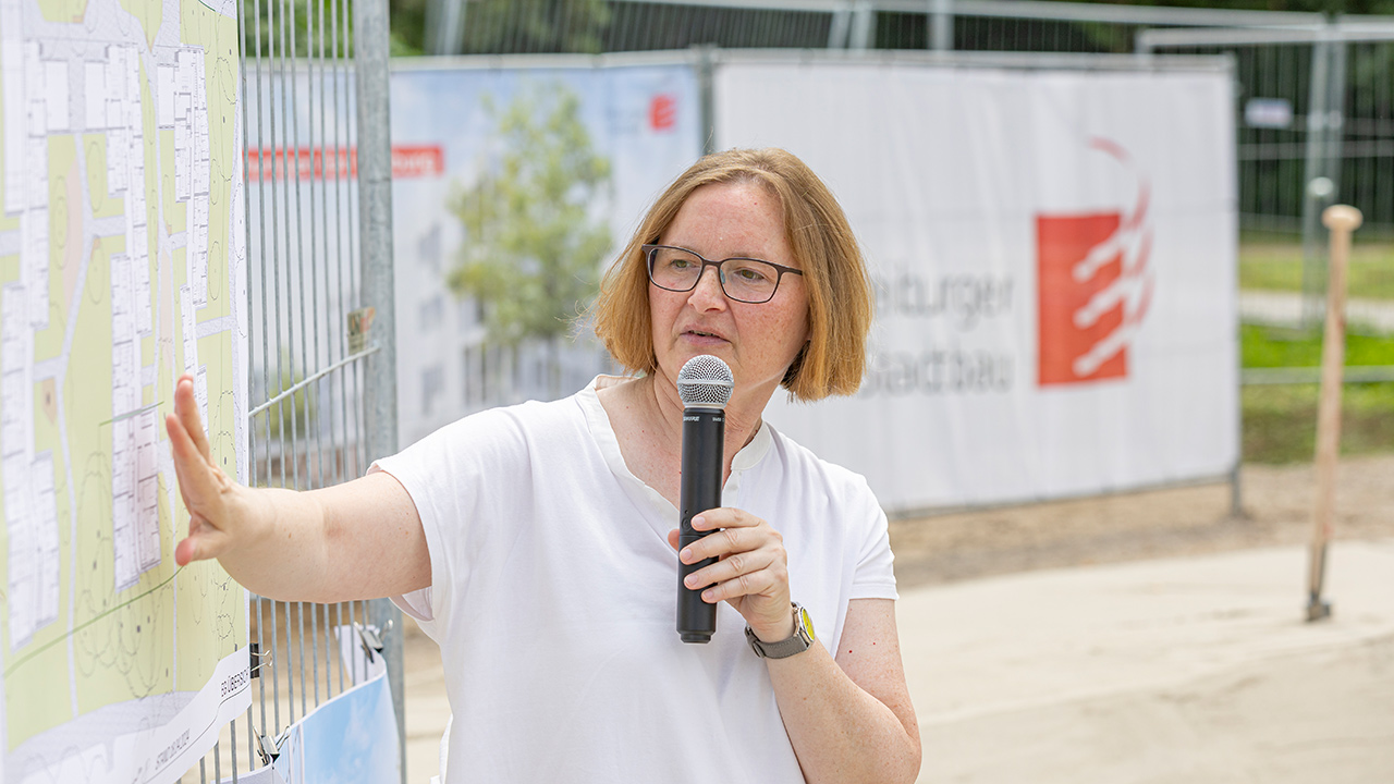 Frau Dr. Szablewska, technische Geschäftsführerin, halt eine Rede und zeigt dabei auf einem Bauplan